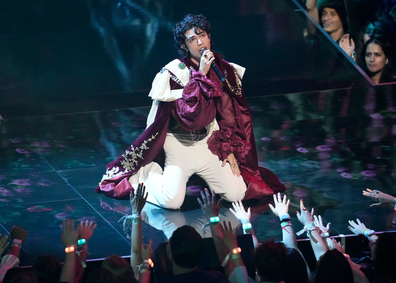 A musician sings on stage while people reach their arms toward him.