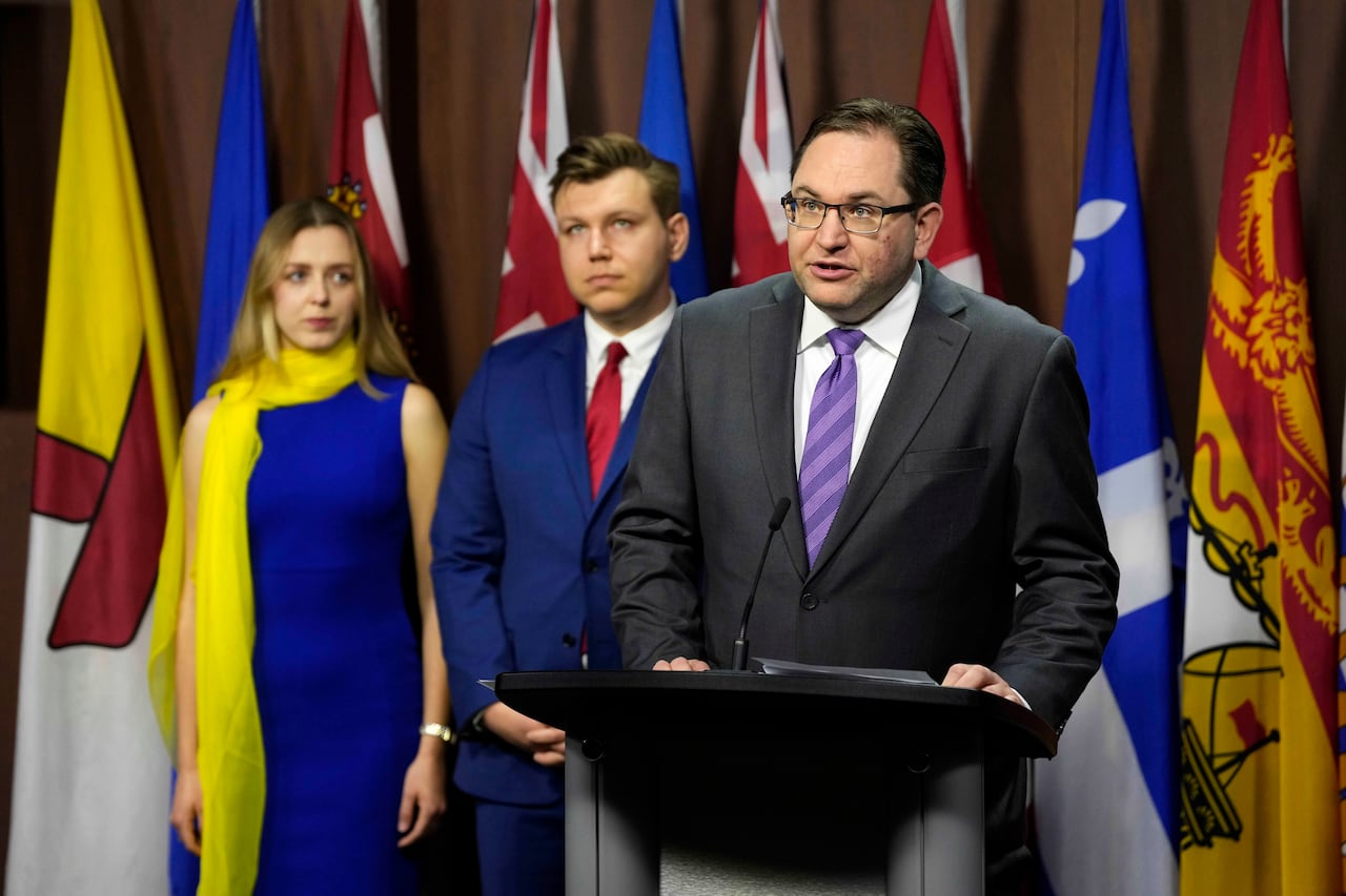 A man in a suit standing at a podium in front of some flags.