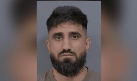 A mugshot of a man with a beard in front of grey background