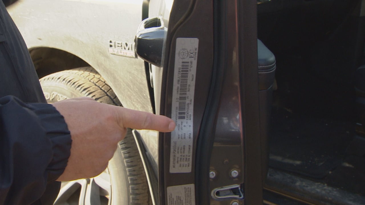 A hand points to a white sticker on the inside of a vehicle door.