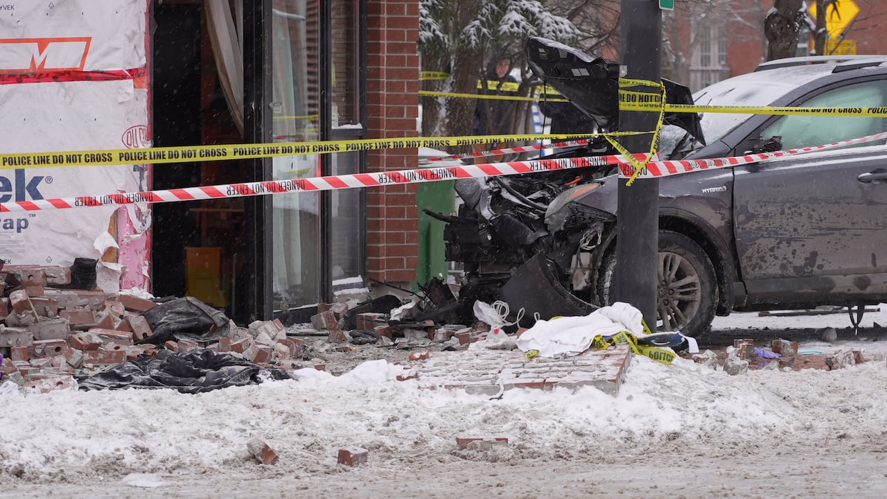 The damaged front of a vehicle that crashed into a brick building on a snowy morning.