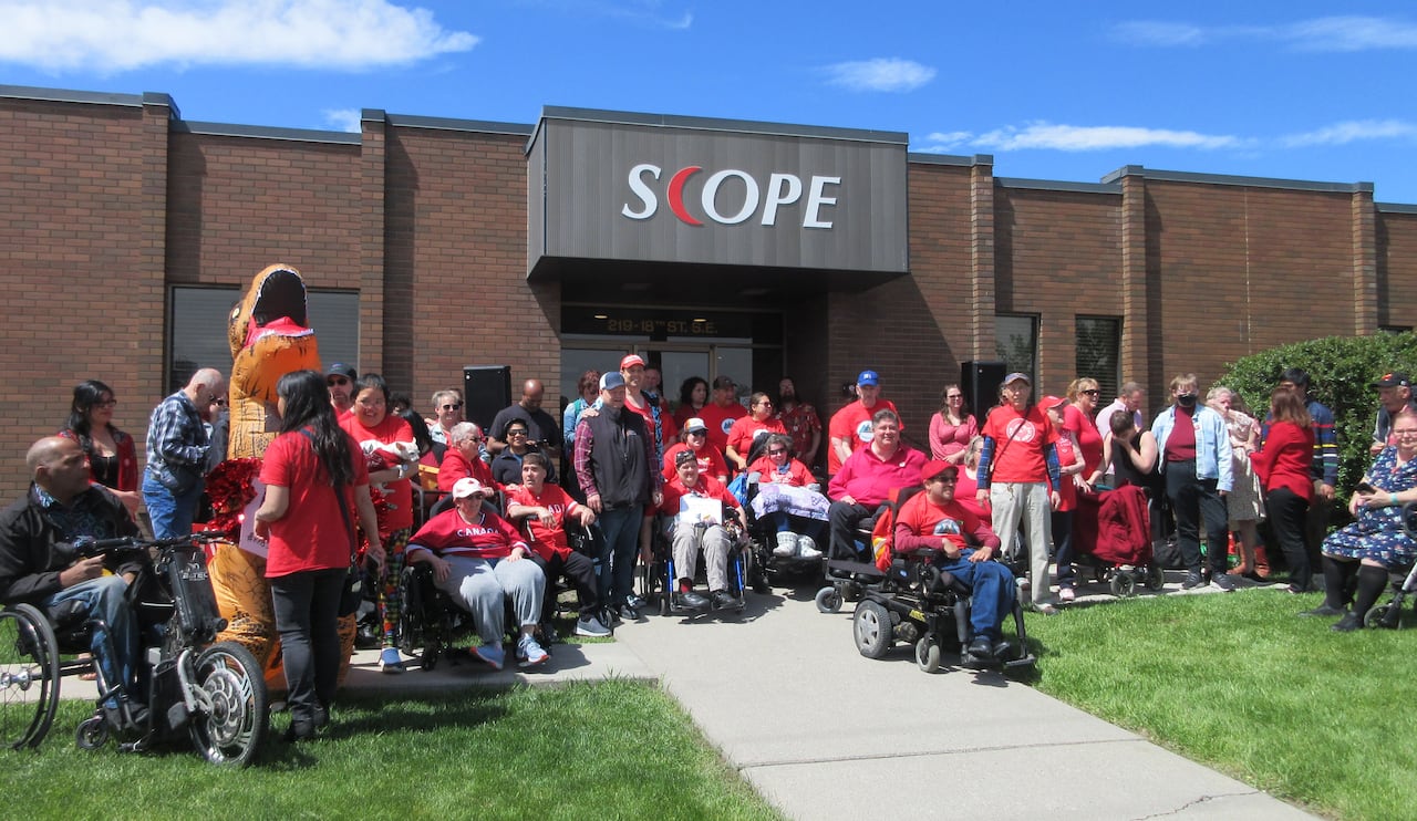 A big group of people wearing red t-shirts gather on the lawn outside of a building that says "SCOPE."
