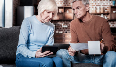 An upset couple sitting down looking at papers.