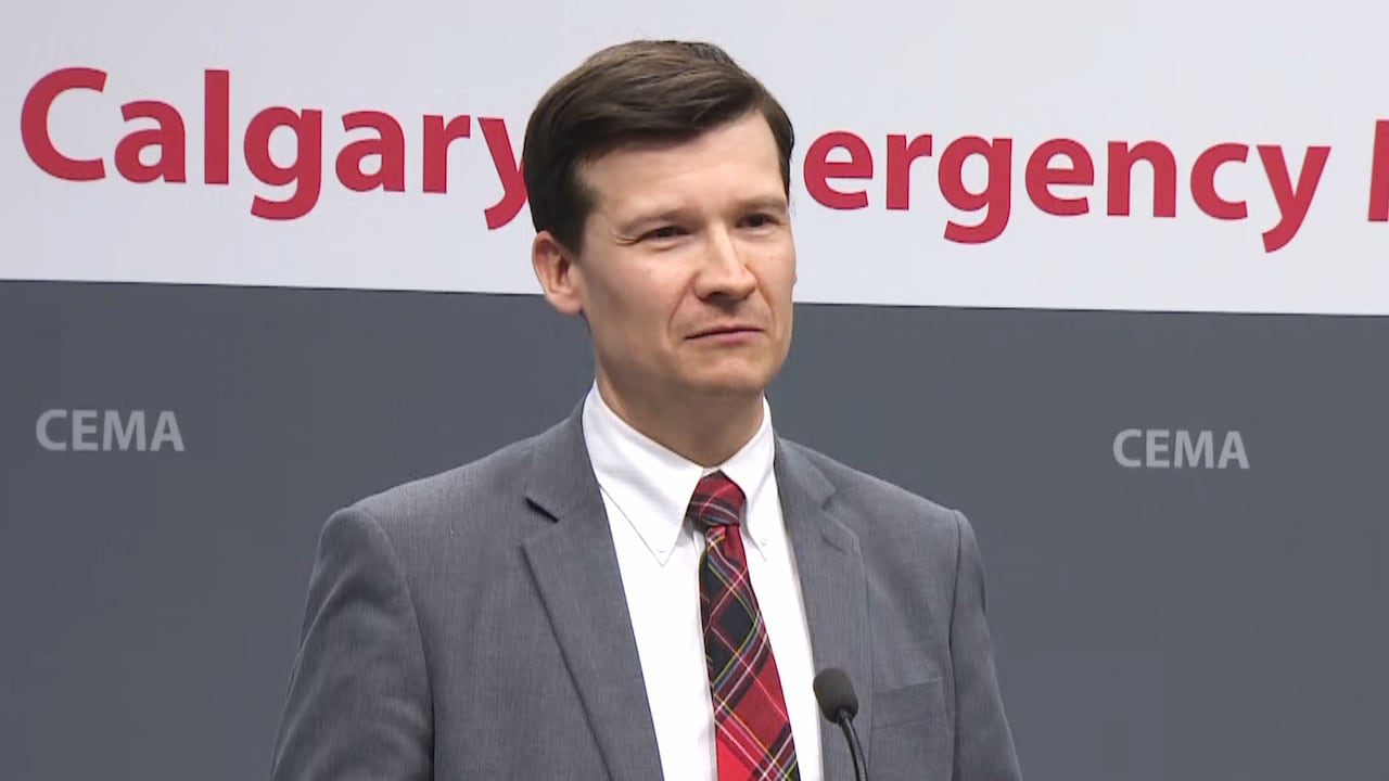 A man in grey suit with a tartan tie holds a press conference. 