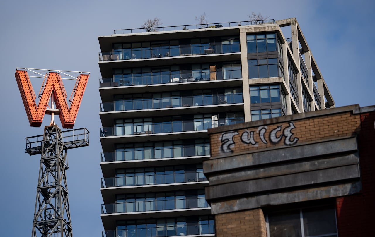 A large 'W' sign on a metallic tower is seen with a skyscraper and a wall next to it.