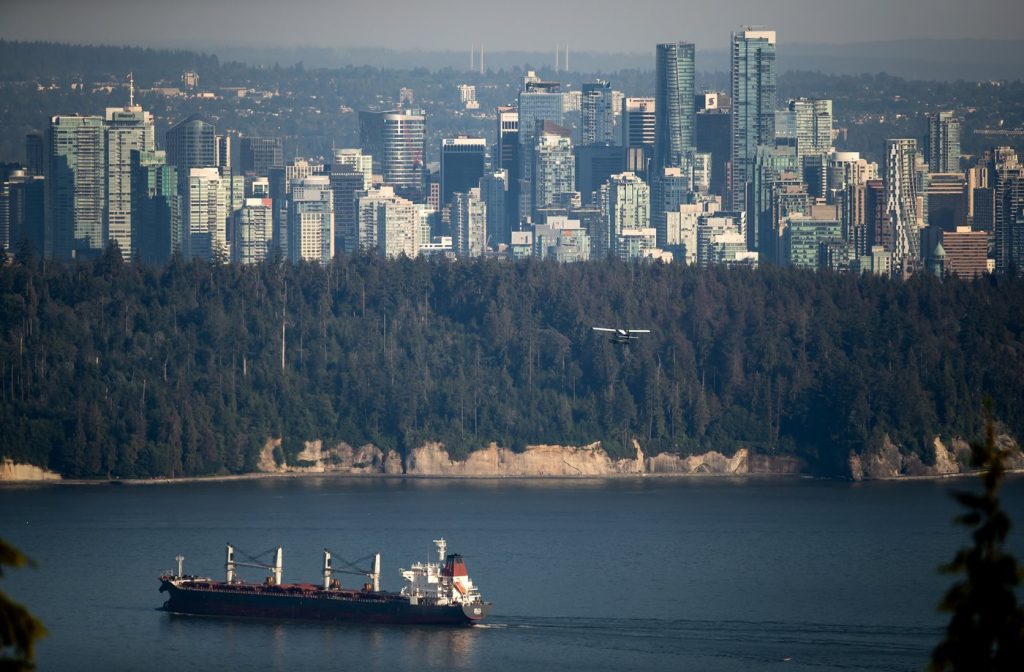 A bulk carrier cargo ship travels into port as a Harbour Air seaplane flies towards Stanley Park and the downtown skyline in Vancouver on Wednesday, July 27, 2022. THE CANADIAN PRESS/Darryl Dyck