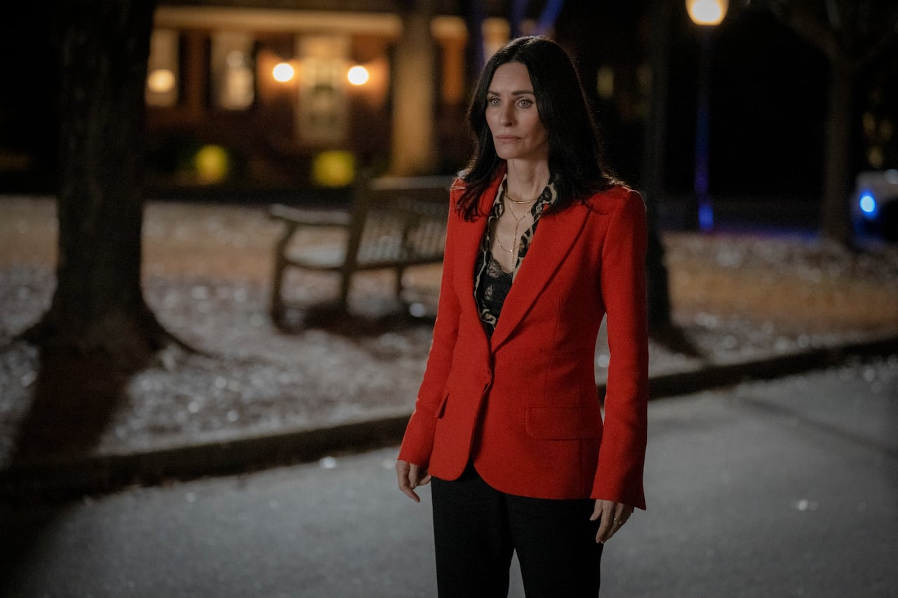 A woman wearing a red blazer stands in a street at night. 
