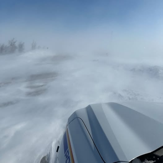 The front corner of an RCMP cruiser facing a blustery highway covered in snow.