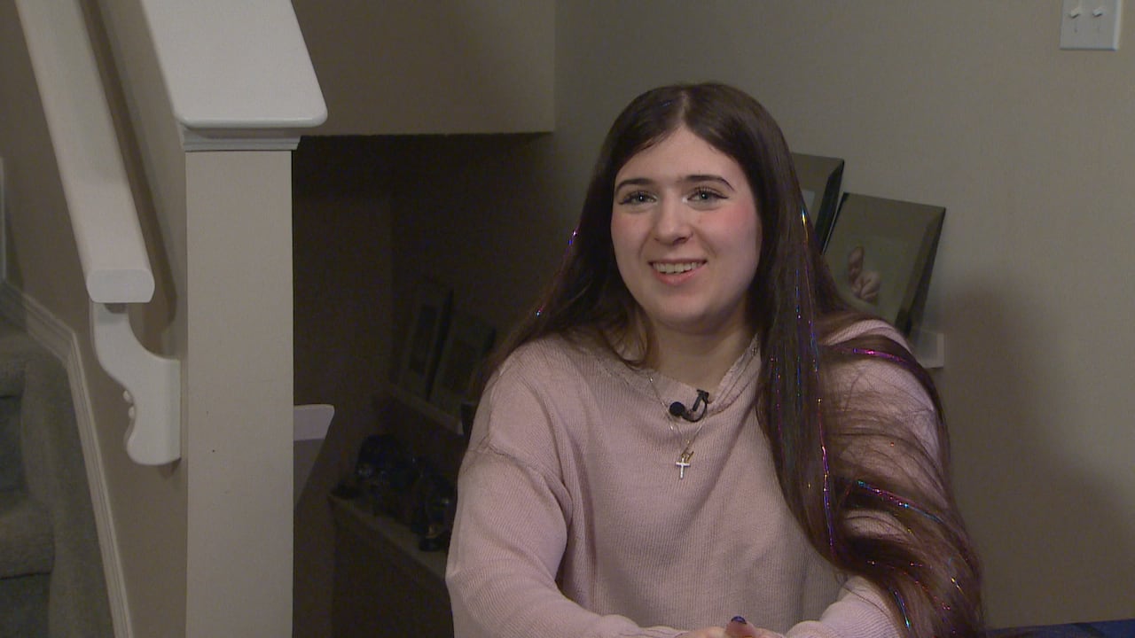 A girl sitting in a pink sweater smiling.