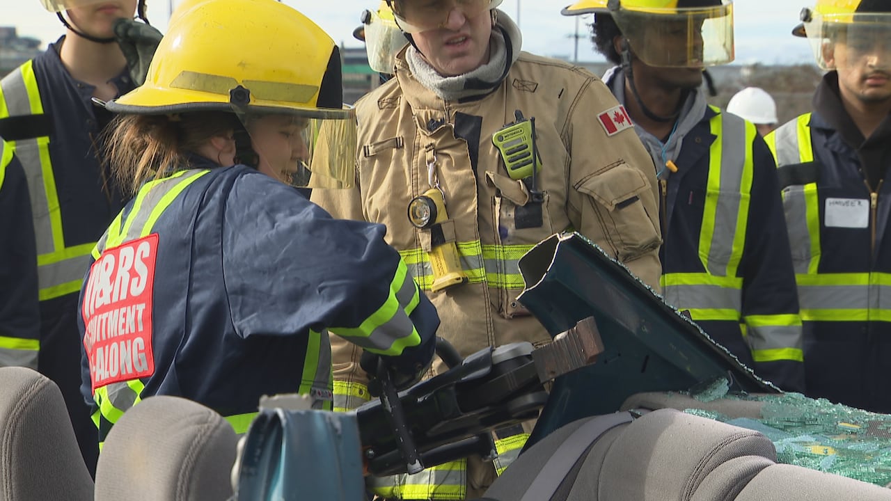 A girl uses a large metal instrument to deform a car.