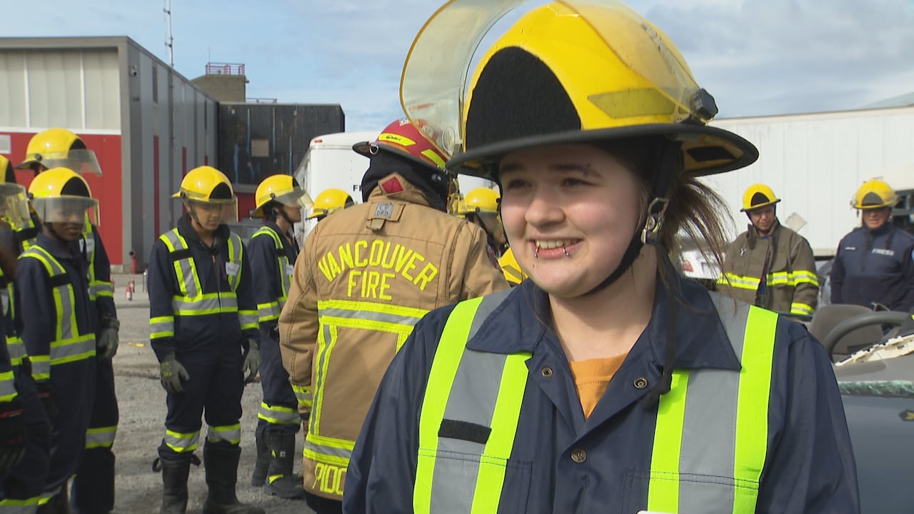 A girl smiles with firefighters visible behind her.