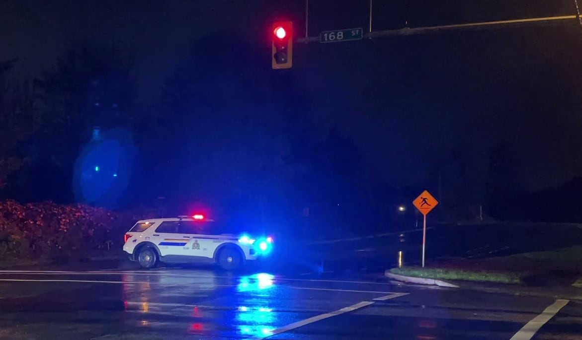 A police car with flashing lights blocks off an intersection at night.