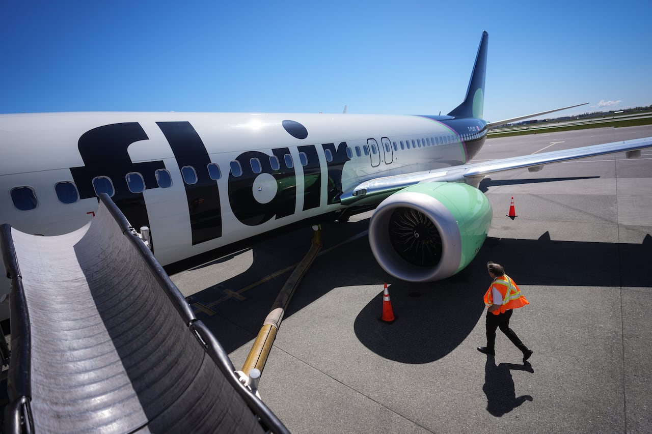 An airline captain in an orange safety vest inspects the outside of a Flair Airlines plane