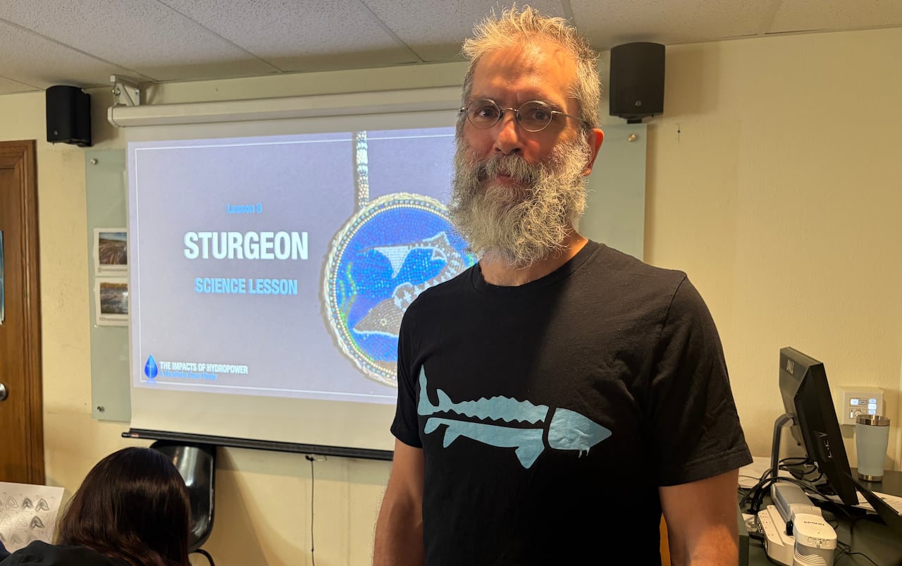 A man in a classroom. He's wearing a shirt with a sturgeon.