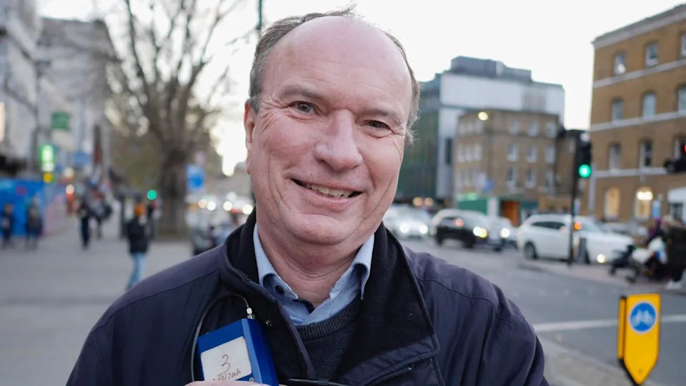Prof Jonathan Grigg, eyes to camera, stands next to busy main road