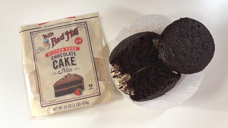 Bag of Bob's Red Mill Gluten Free chocolate cake mix on table next to chocolate cupcakes