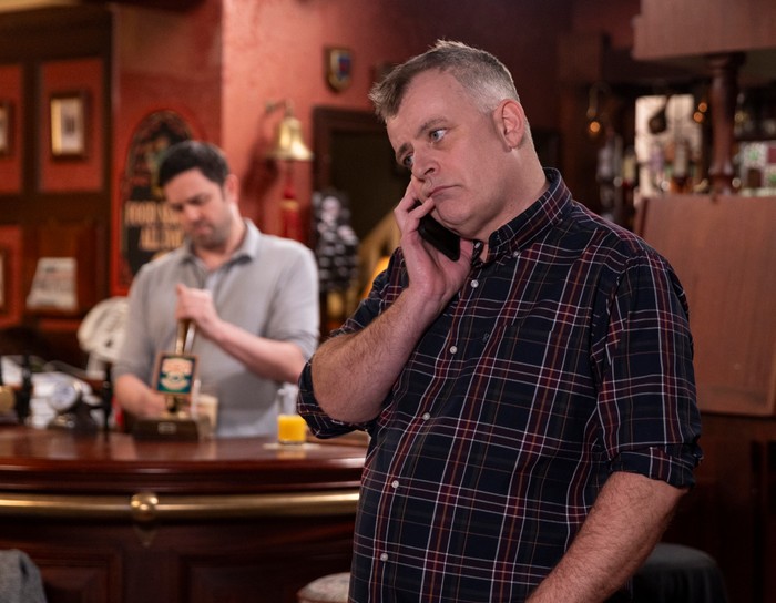 23_02_coro_steve_01 Steve on the phone in the Rovers, with Ben serving a customer behind in a scene from Coronation Street