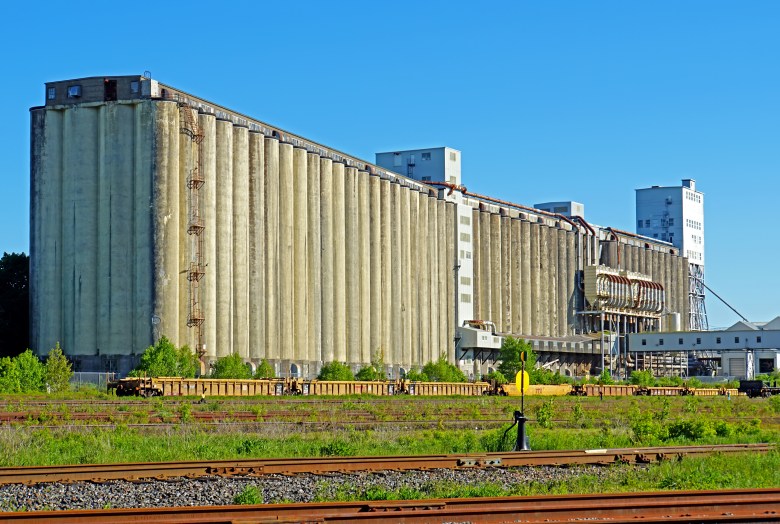 Grain elevators against a clear blue sky, with several sets of railway tracks in the foreground.