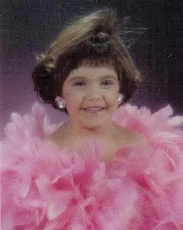A little girl in big earrings and a fluffy pink feather boa.