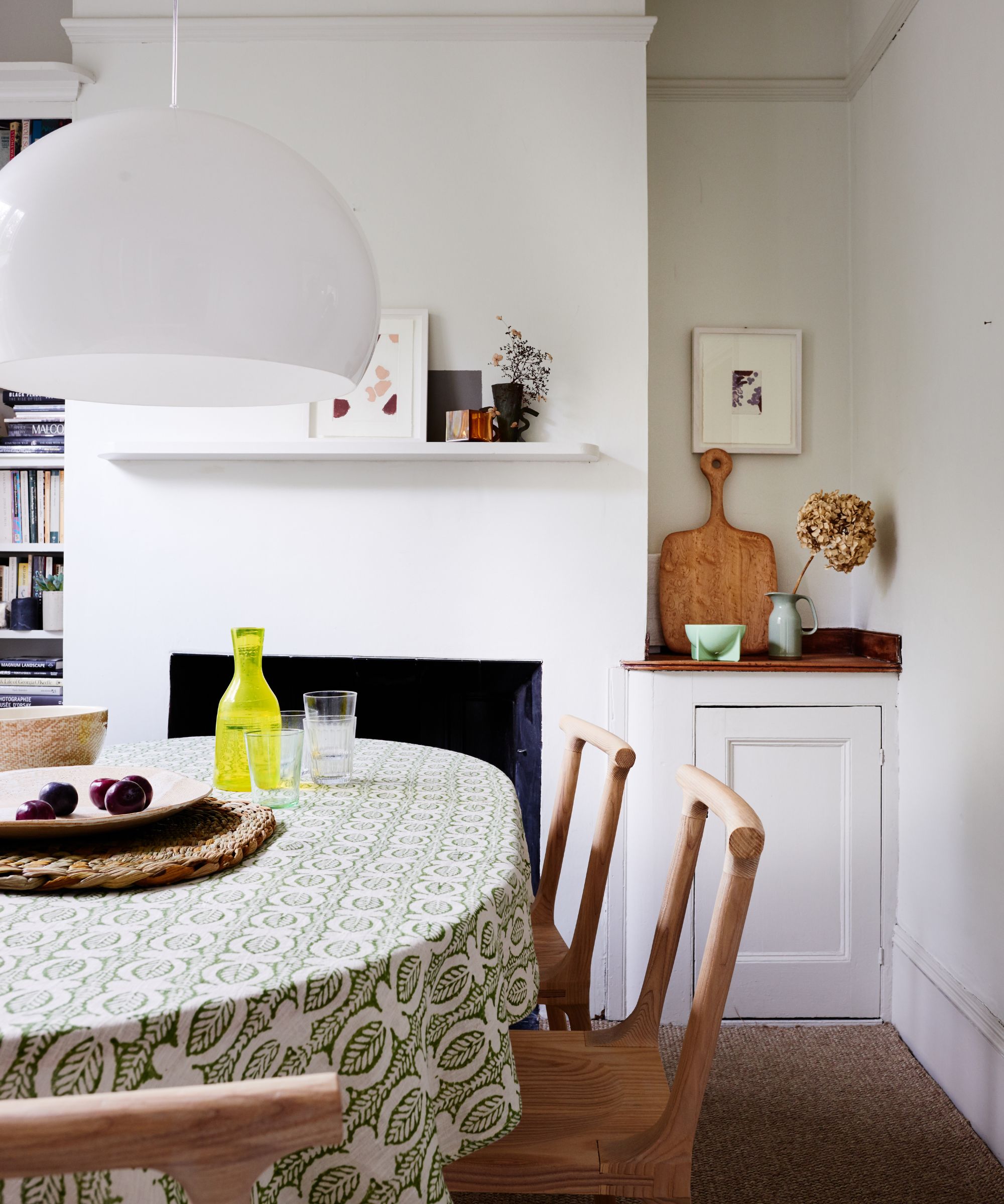Breakfast nook with wooden dining chairs, table with green and white tablecloth, glass pendant light, and white walls