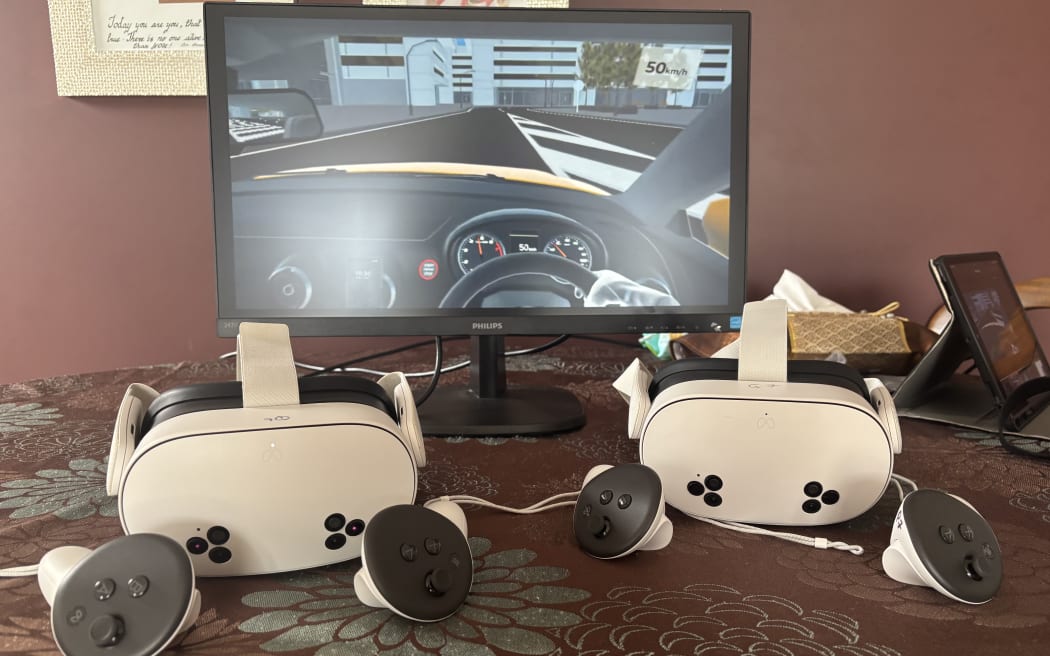 Two sets of VR headsets and controllers in front a computer screen showing the virtual reality driving simulator