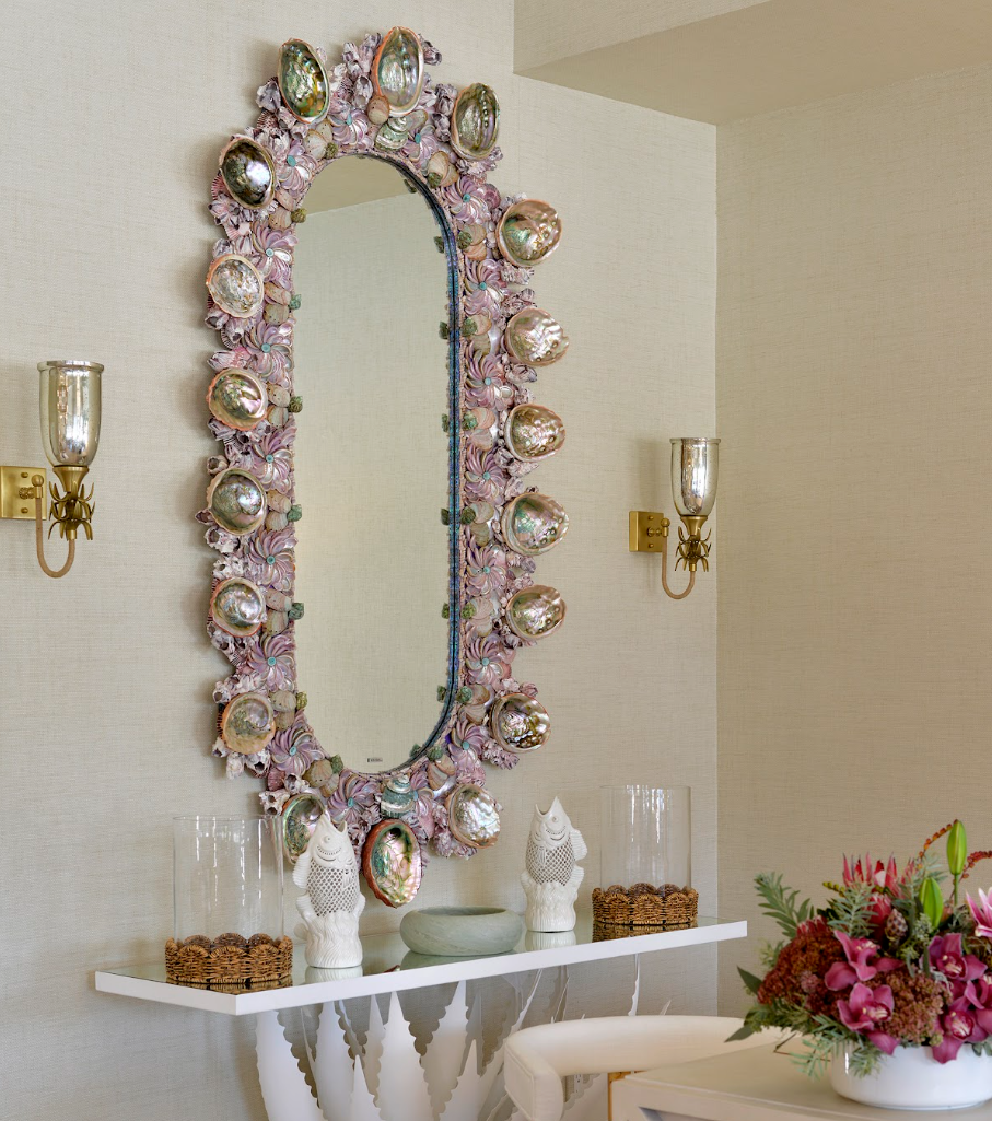 Decorative wall mirror with shell motif, accompanied by sconces and a console table.
