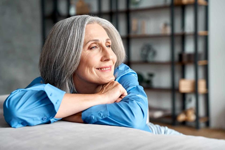 Happy relaxed mature old woman resting dreaming sitting on couch at home. Smiling mid aged woman relaxing. Peaceful serene grey-haired lady feeling peace of mind enjoying lounge on sofa and thinking.