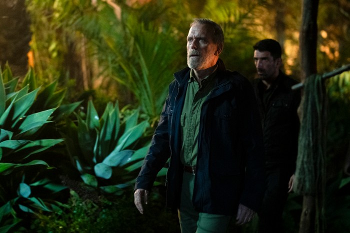 547915,TITLE: The Night Manager S2 Hugh Laurie stars in The Night Manager season 2; in this scene, Roper is walking in a forest setting, looking dismayed by something