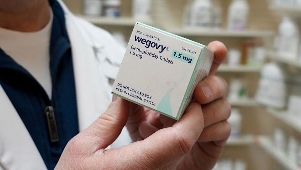 A close-up of a pharmacist holding a box of Wegovy weight-loss pills in a pharmacy