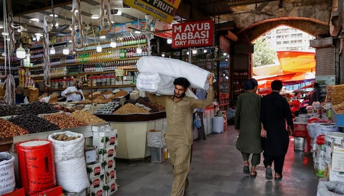 A man walks with sacks of supplies on his shoulder to deliver to a nearby shop at a market in Karachi, June 11, 2024. — Reuters