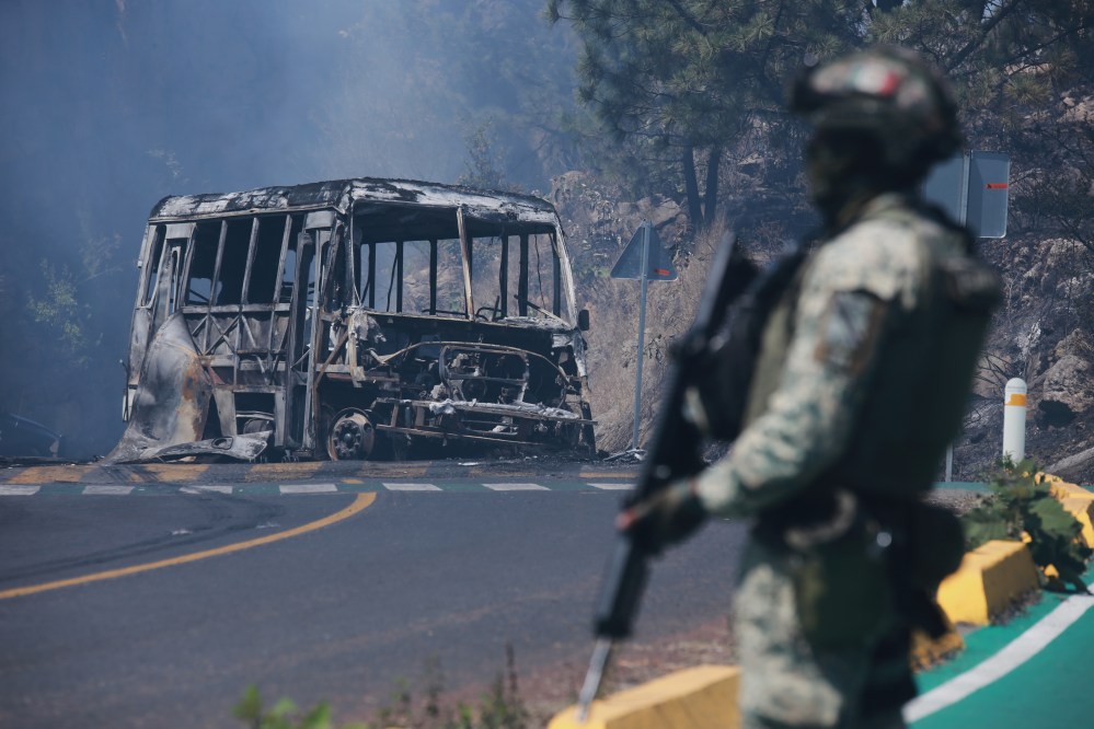 A soldier stands guard by a charred vehicle after it was set on fire, in Cointzio, Michoacán state, Mexico, Sunday, Feb. 22, 2026, following the death of the leader of the Jalisco New Generation Cartel, Nemesio Oseguera, known as