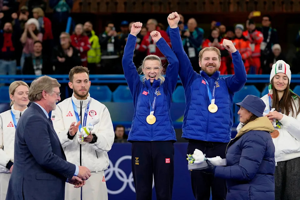Feb 10, 2026; Cortina d'Ampezzo, Italy; Gold medalists Isabella Wranaa and Rasmus Wranaa of Sweden celebrate during the medal ceremony for the curling mixed doubles gold medal game during the Milano Cortina 2026 Olympic Winter Games at Cortina Curling Olympic Stadium. On the left is golf course architect Beau Welling, who is the president of the World Curling Federation. Mandatory Credit: Michael Madrid-Imagn Images