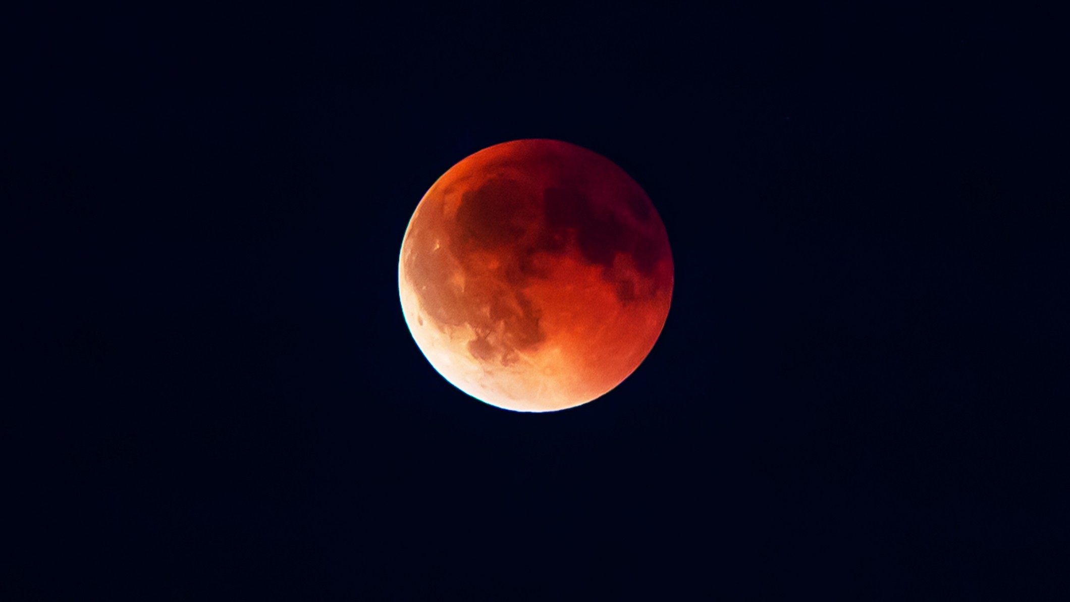 blood red moon against a black background the lower left of the moon is a lighter shade of red.