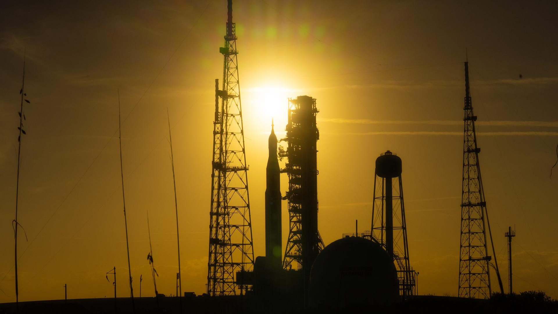 A silhouette of a rocket surrounded by scaffolding is seen in a dim yellow sunset
