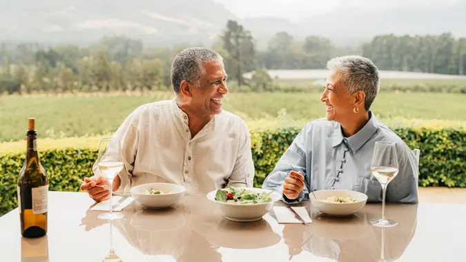 A rich couple sitting at a table together looking at each other while eating lunch at a vineyard