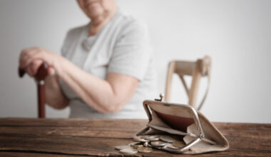 An older person sitting at the table with a wallet full of coins in front of them.