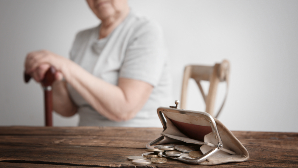 An older person sitting at the table with a wallet full of coins in front of them.
