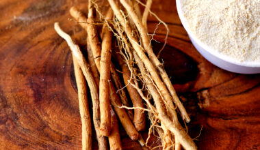 Ashwagandha roots and a white powder known as Withania somnifera in a white bowl on a wooden table.