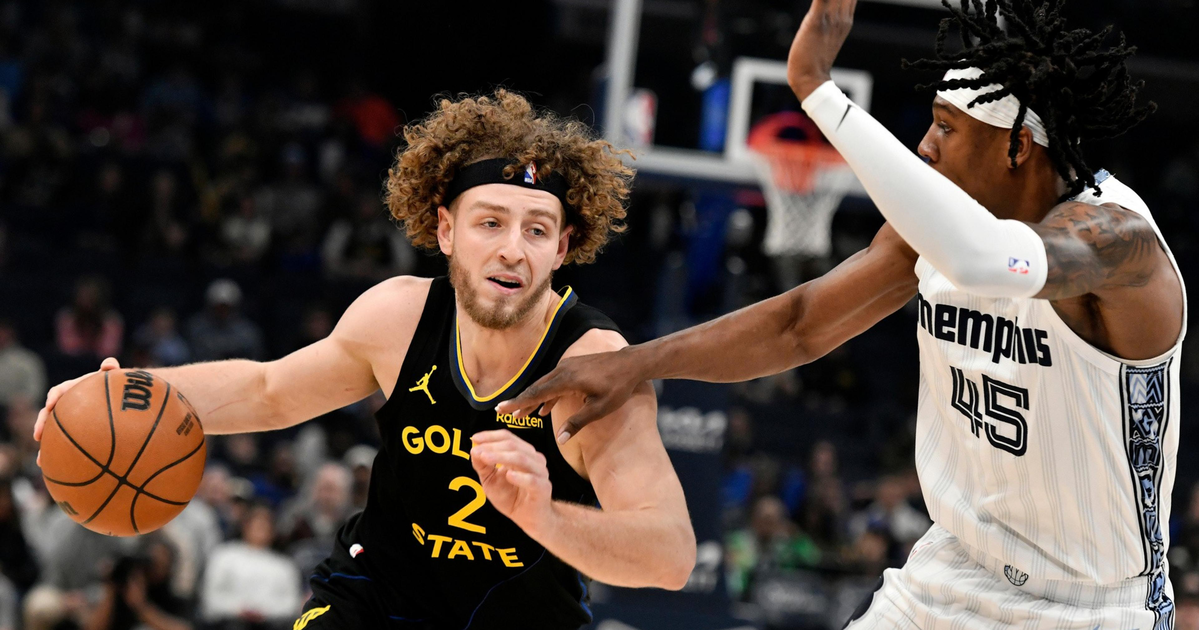 A Golden State player with curly hair drives past a Memphis defender wearing white, both focused intensely as they compete near the basket.