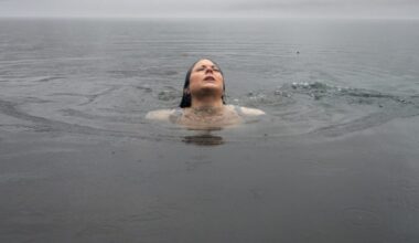 A woman swimming in water emerges from the surface with her eyes closed.
