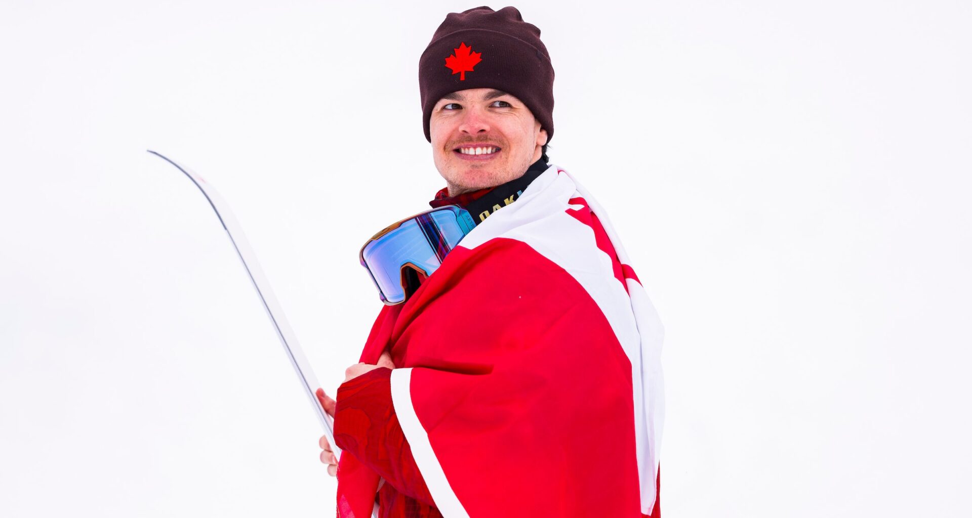 Mikaël Kingsbury of Team Canada celebrates after winning the silver medal in freestyle ski moguls at the Milano Cortina 2026 Olympic Winter Games, smiling in the finish area with the snowy course behind him.