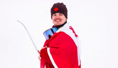 Mikaël Kingsbury of Team Canada celebrates after winning the silver medal in freestyle ski moguls at the Milano Cortina 2026 Olympic Winter Games, smiling in the finish area with the snowy course behind him.
