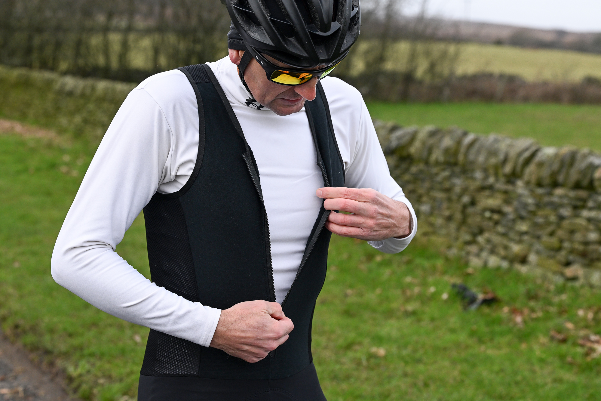 Man zipping up some black winter bibs wearing a white base layer and black helmet