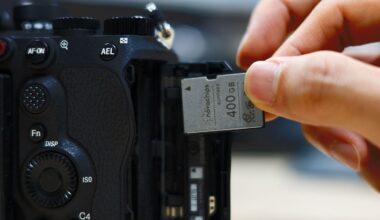 A hand inserts a 400GB memory card into the open memory card slot of a black digital camera.
