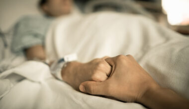 Man holding hand, giving support and comfort to woman, loved one sick in hospital bed.