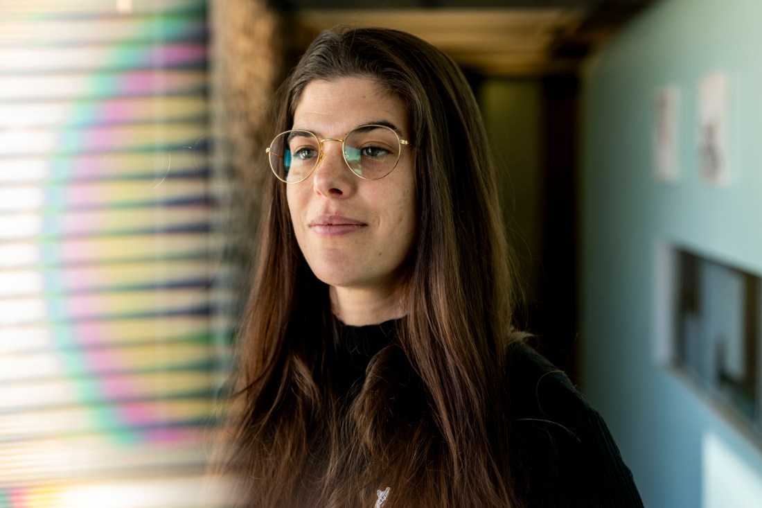 Portrait of Maddalena Torricelli wearing a dark long-sleeve shirt and glasses, standing in a hall with turquoise walls. 