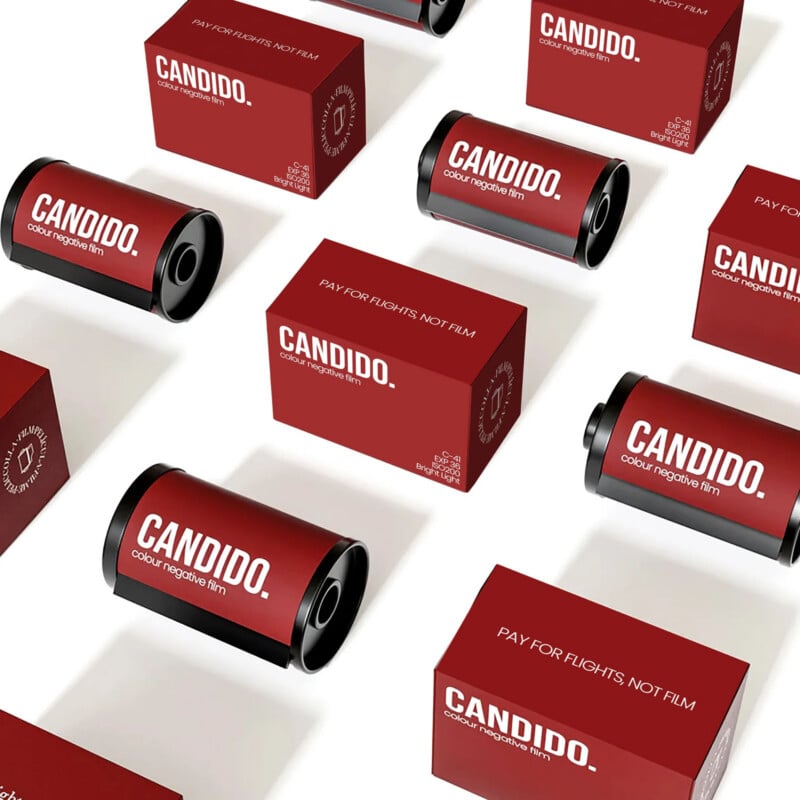 Red boxes and black film canisters arranged diagonally on a white surface. The boxes and canisters are labeled “CANDIDO. color negative film.” One box reads, “PAY FOR FLIGHTS. NOT FILM.”.