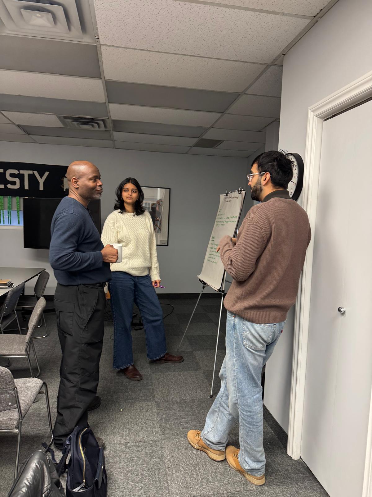 Three people are standing in conversation. There are two men and a woman.