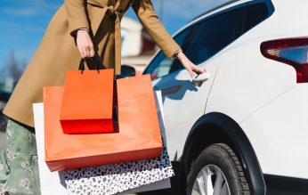 Person holding multiple shopping bags while opening a car door
