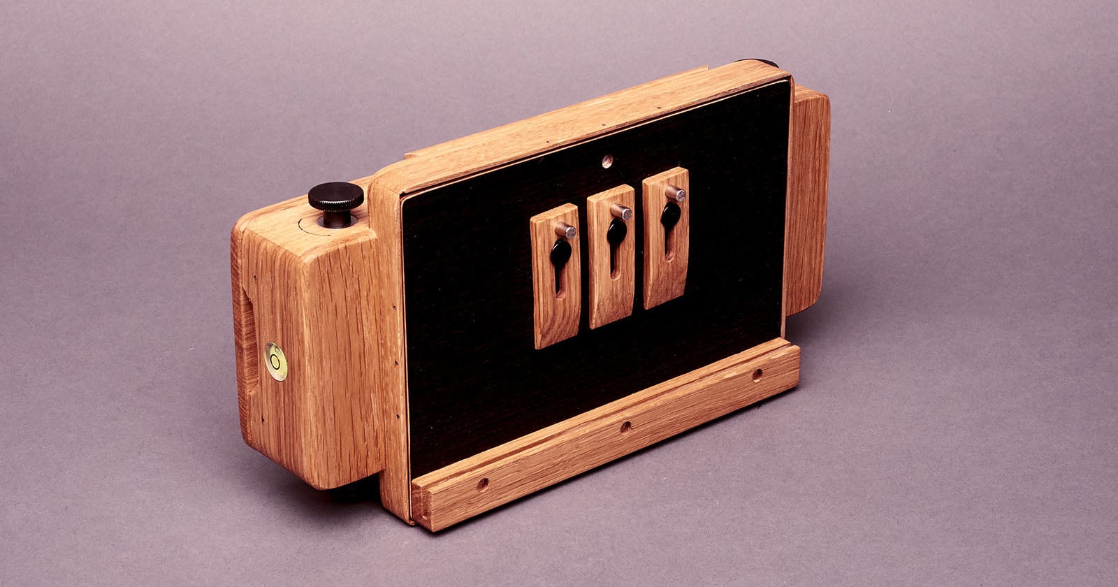 A handcrafted wooden camera with black panels and three toggle switches on the front, placed on a plain background. The design combines natural wood with functional hardware elements.